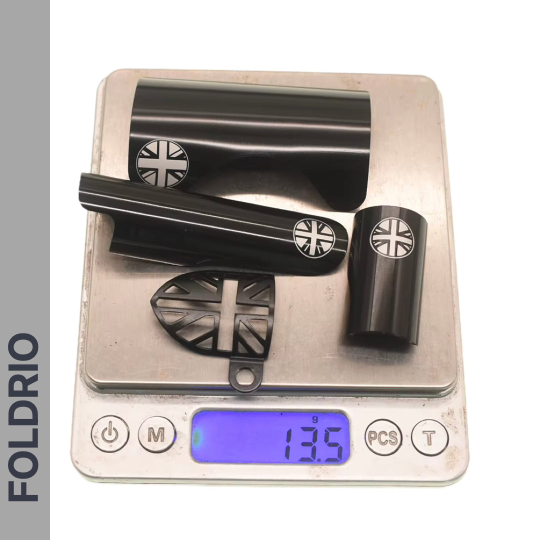A set of four black FOLDRIO Brompton Frame Protectors with white British flag designs is shown on a digital scale reading 135g, placed on a white surface with "FOLDRIO" written vertically on the left.