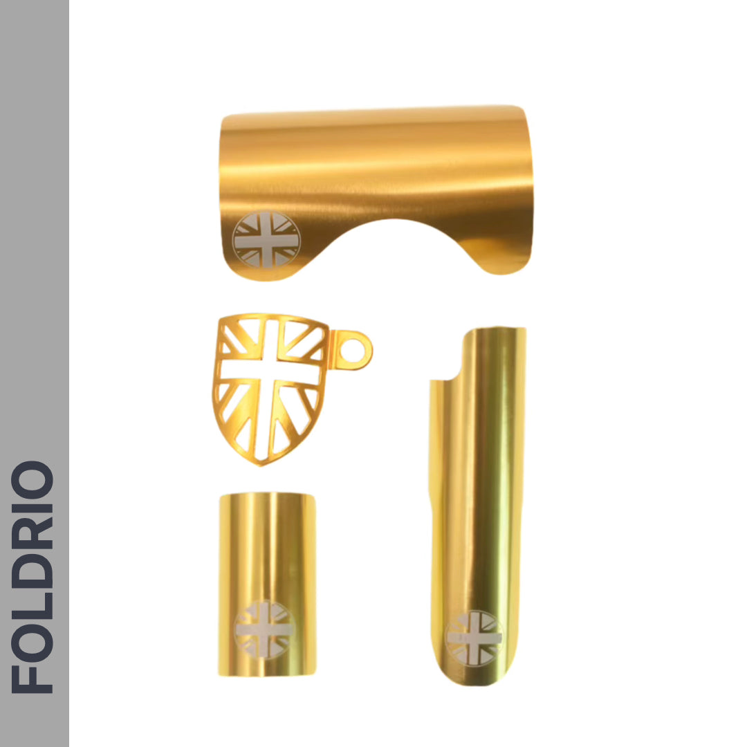 Four gold metal Brompton Frame Protector Set with British Flag cutouts by FOLDRIO—including shield-shaped chainstay guard and rear fork cover—are shown on a white background with “FOLDRIO” vertically on a gray bar at left.
