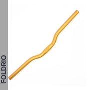 The Brompton M Handlebar – Anodised Aluminium (shown in gold) features a slight rise and ergonomic bends for upright riding. On a white background, "FOLDRIO" appears vertically on a gray strip along the left side.