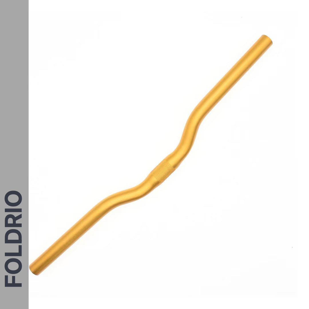The Brompton M Handlebar – Anodised Aluminium (shown in gold) features a slight rise and ergonomic bends for upright riding. On a white background, "FOLDRIO" appears vertically on a gray strip along the left side.
