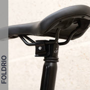 Close-up of a black bicycle seat on a Brompton Titanium Seatpost – Lightweight Upgrade, 560mm & 580mm (31.8mm diameter), with FOLDRIO written vertically on the left side against a gray background.