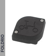 The Brompton AirTag Saddle Mount – Hidden Tracker Holder is a black, curved plastic accessory with two screws and a bicycle icon engraved on top. “FOLDRIO” is vertically shown on a gray sidebar to the left.