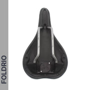 The image shows the underside of a black bicycle seat with metal rails and a mounting area. A Brompton AirTag Saddle Mount – Hidden Tracker Holder is subtly integrated, with FOLDRIO vertically shown on a gray strip along the left side.
