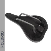A black Brompton AirTag Saddle Mount – Hidden Tracker Holder is shown from the underside, emphasizing metal rails, mounting points, and a concealed AirTag slot. At left, a vertical gray bar displays "FOLDRIO" in bold dark letters.