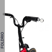A close-up of a black folding bicycle handlebar with a bell, brake lever, and Brompton Bar End Mirror – 360° Adjustable, Foldable attached to a red bike frame. "FOLDRIO" appears vertically on a gray side banner against a white background.