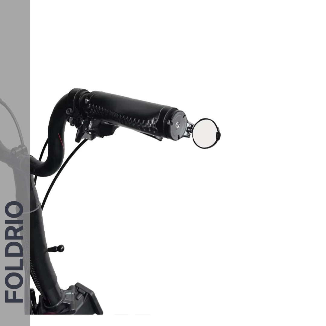 Close-up of a black bicycle handlebar fitted with the Brompton Bar End Mirror – 360° Adjustable, Foldable. "FOLDRIO" appears vertically on a gray strip at the left. The background is predominantly white.