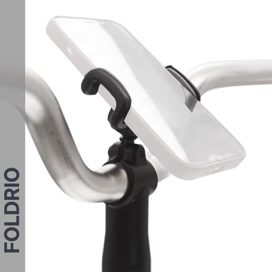 A smartphone is mounted on a bicycle handlebar with the FOLDRIO Brompton Phone Mount – Lightweight, No Case Needed. The word FOLDRIO appears vertically on the left side of the image.