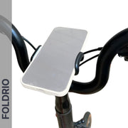A smartphone sits horizontally on the Brompton Phone Mount – Lightweight, No Case Needed by FOLDRIO, secured by a black adjustable bike phone holder. The word FOLDRIO is displayed vertically on the left side of the image.
