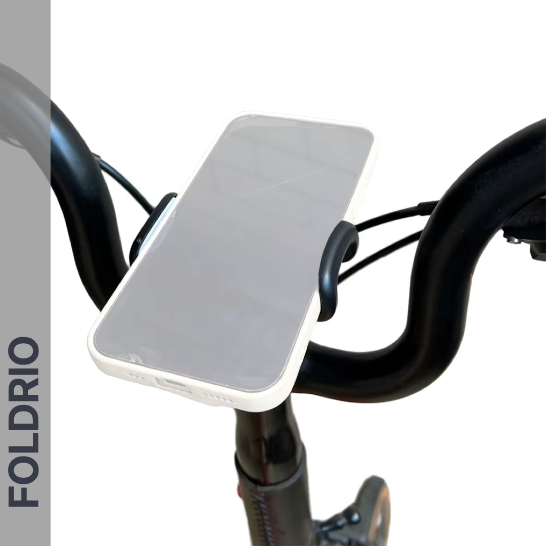 A smartphone sits horizontally on the Brompton Phone Mount – Lightweight, No Case Needed by FOLDRIO, secured by a black adjustable bike phone holder. The word FOLDRIO is displayed vertically on the left side of the image.