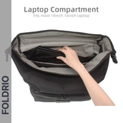 A hand places a laptop into the inner compartment of the black and gray FOLDRIO Brompton Roll-Top Front Bag – 27.5L. Text reads: Laptop Compartment: Fits most 14-inch & 16-inch laptops. 'FOLDRIO' appears vertically on the left.