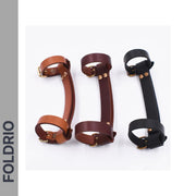 Three Brompton Leather Carry Handles by FOLDRIO, crafted from full-grain leather with brass hardware in brown, dark brown, and black, are displayed side by side. "FOLDRIO" appears vertically on a gray strip to the left.