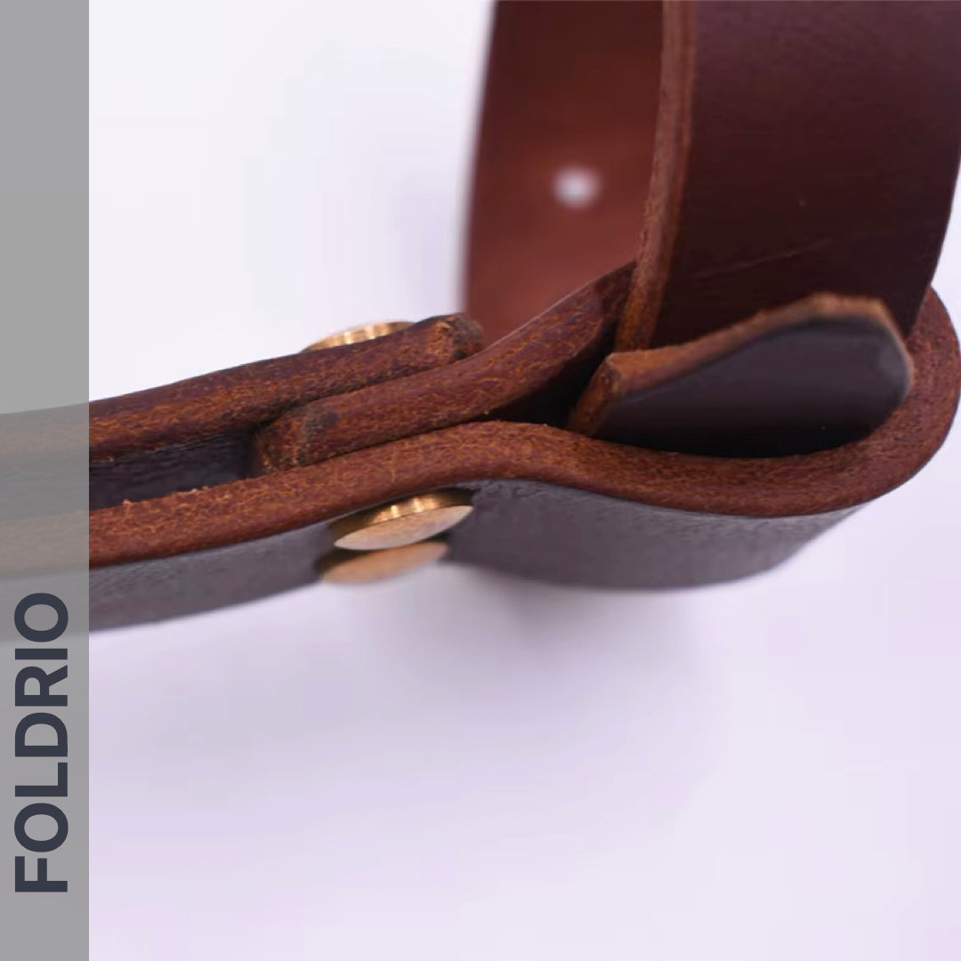 Close-up of the FOLDRIO Brompton Leather Carry Handle, made with full-grain leather and brass hardware, set against a light background. The brand name FOLDRIO appears vertically along the left edge.