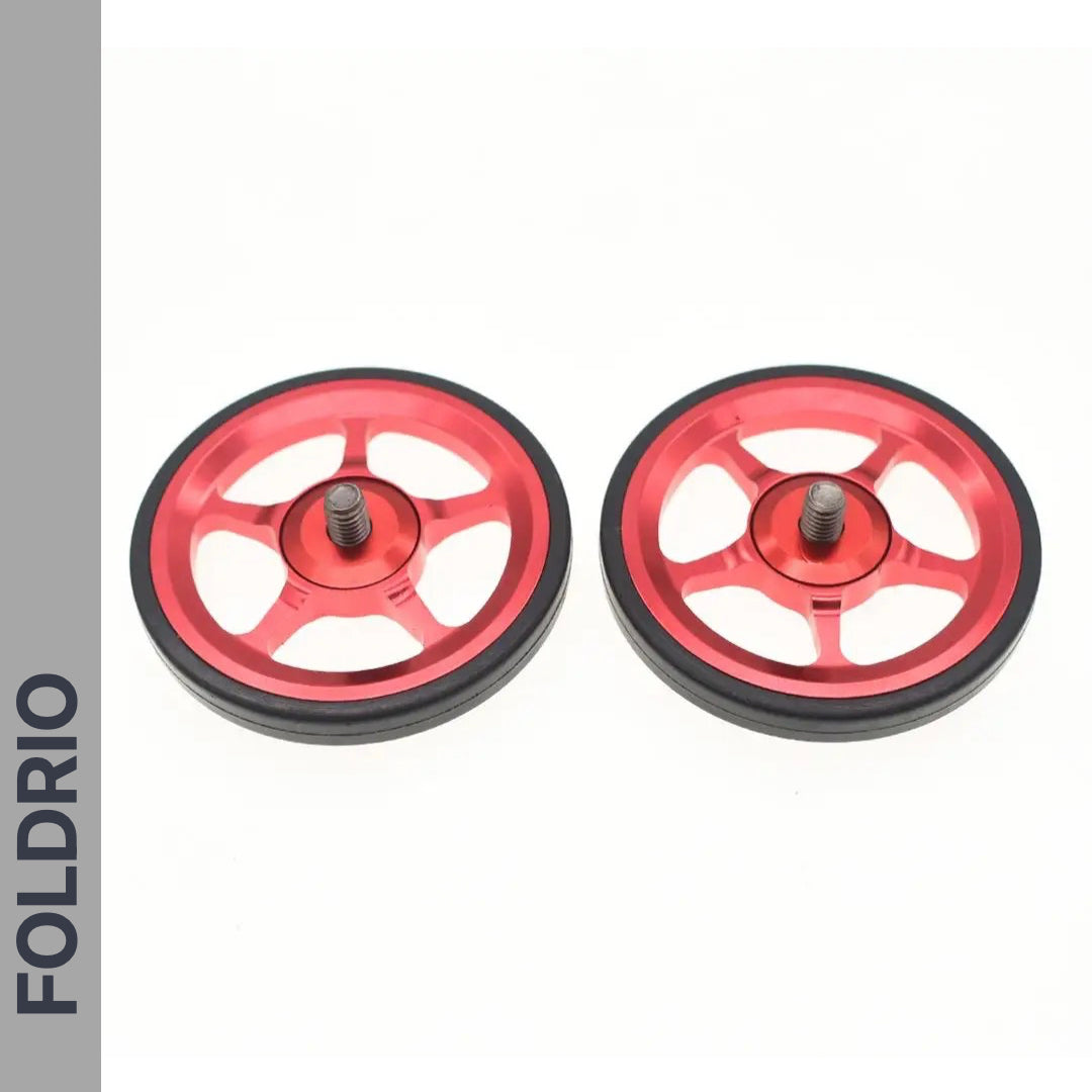 Two red metal Brompton Easy Wheels with black rubber edges and titanium bolts by FOLDRIO are displayed side by side on a white background. The FOLDRIO brand name appears vertically along the left.