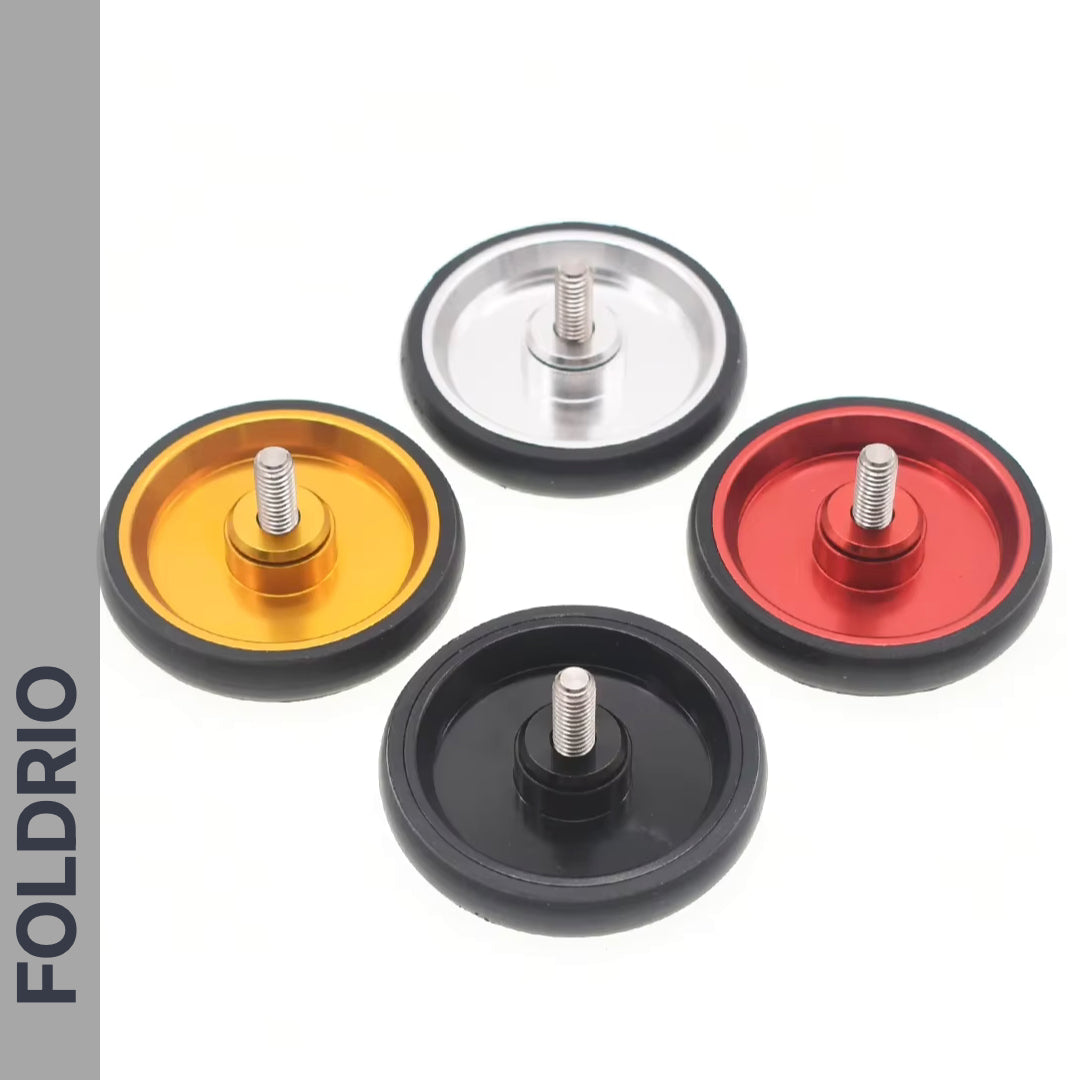 Four circular Brompton Easy Wheels Union Jack Edition by FOLDRIO, in gold, silver, red, and black with titanium bolts, are displayed on a white background. "FOLDRIO" is shown vertically on the left. Perfect for Brompton bikes.