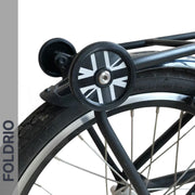 A close-up shows a bicycle’s rear wheel fitted with FOLDRIO Brompton Easy Wheels Union Jack Edition with titanium bolts. "FOLDRIO" appears vertically on a grey strip to the left.