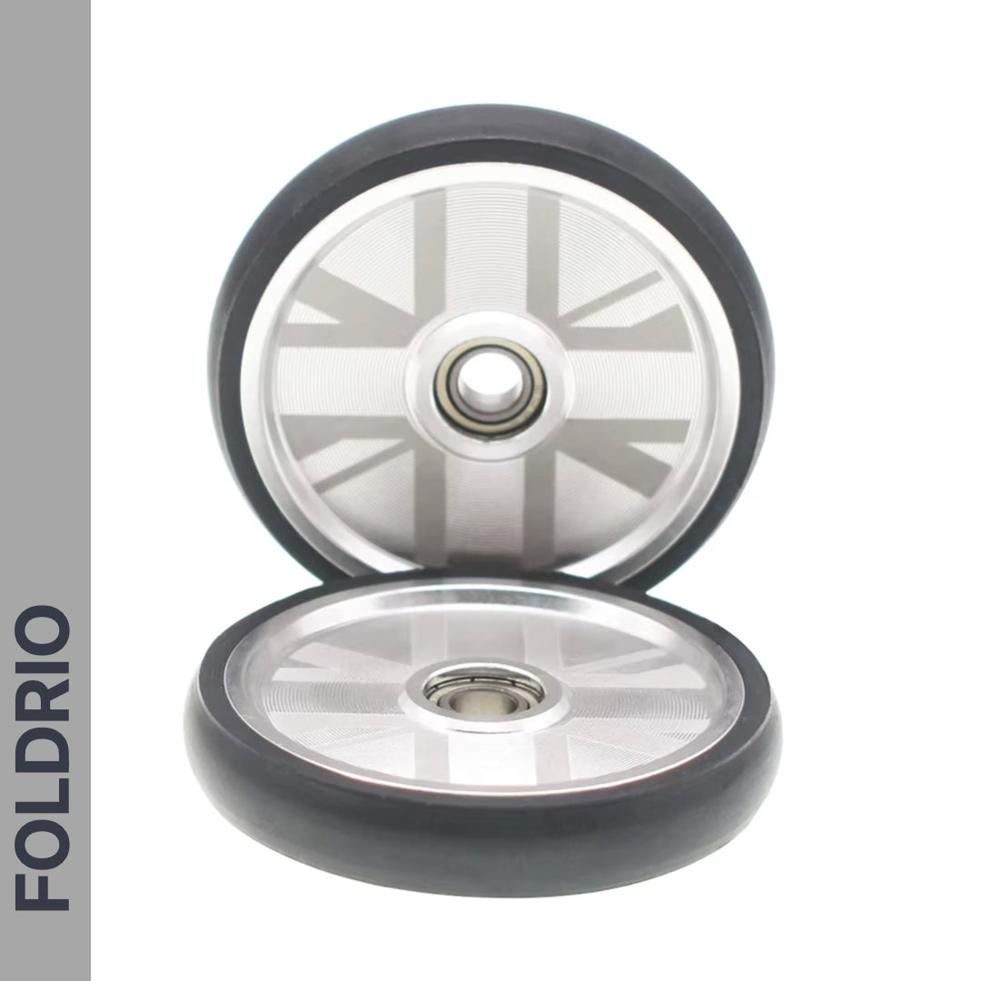 Two Brompton Easy Wheels Union Jack Edition by FOLDRIO, featuring titanium bolts, are shown on a white background. The word FOLDRIO is vertically displayed on a gray strip to the left.
