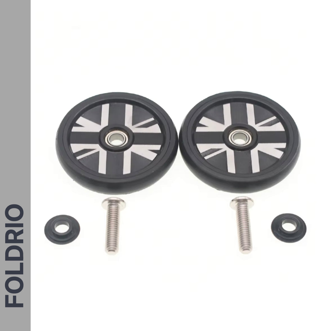 Two small black Brompton Easy Wheels Union Jack Edition with titanium bolts by FOLDRIO and two washers are displayed on a white background. A grey vertical strip on the left shows "FOLDRIO" in bold black letters.