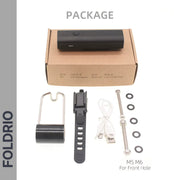 The FOLDRIO Brompton Front Fork Light kit includes a black 400 lumen USB-C rechargeable light, brown box, mounting bracket, USB cable, metal bolts (M5/M6), washers, and rubber spacers. Text: FOLDRIO PACKAGE M5 M6 For Front Hole.