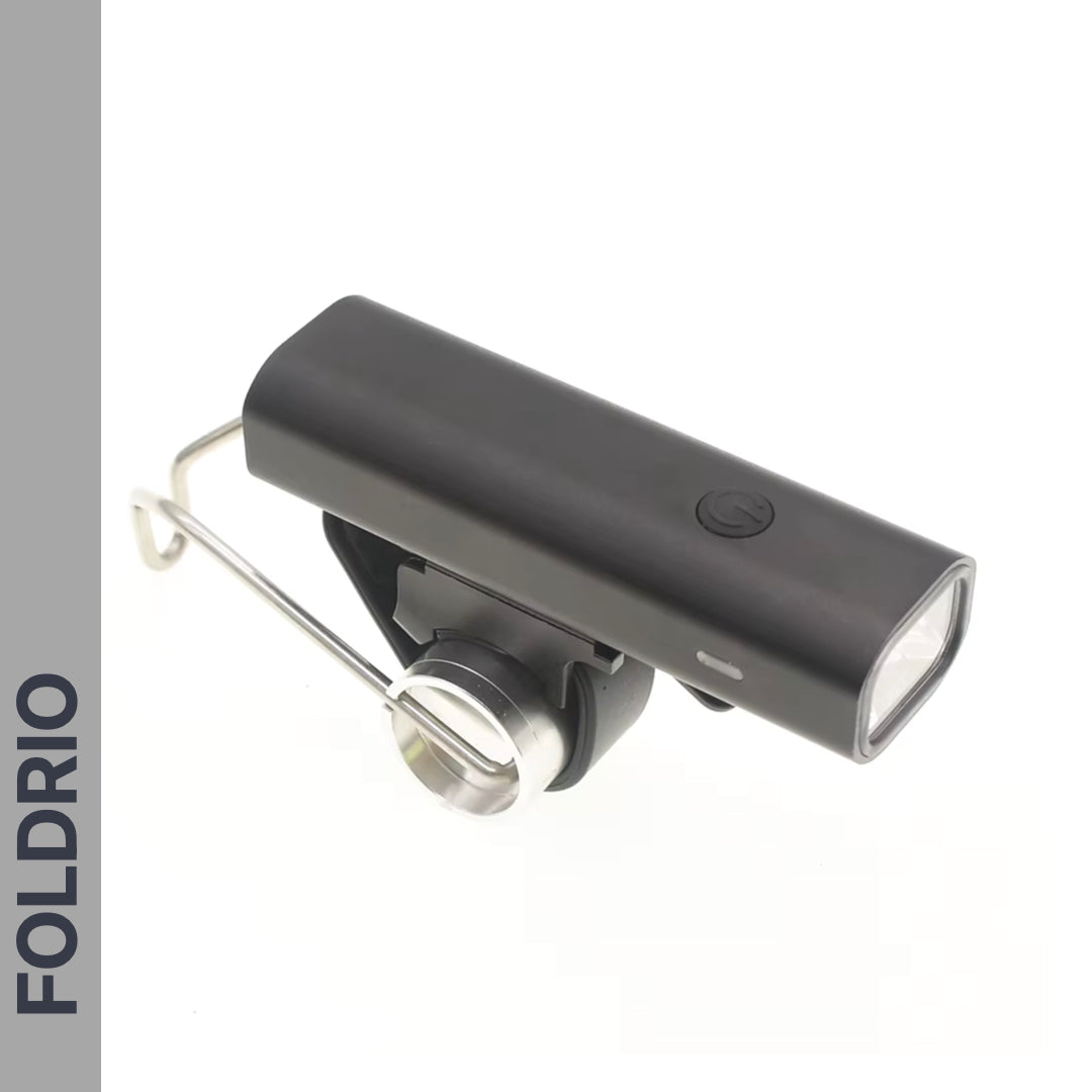 A black, rectangular FOLDRIO Brompton Front Fork Light (400 lumens, USB-C rechargeable) with adjustable beam and top button, plus a metal mounting bracket. Shown on white background with "FOLDRIO" vertically on the left.