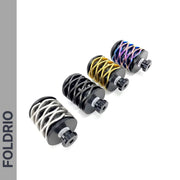 Four cylindrical metal objects, including the FOLDRIO Brompton Rear Shock Absorber with spiral designs in white, gold, and multicolor, are aligned diagonally on a white background. "FOLDRIO" appears vertically on a gray sidebar to the left.