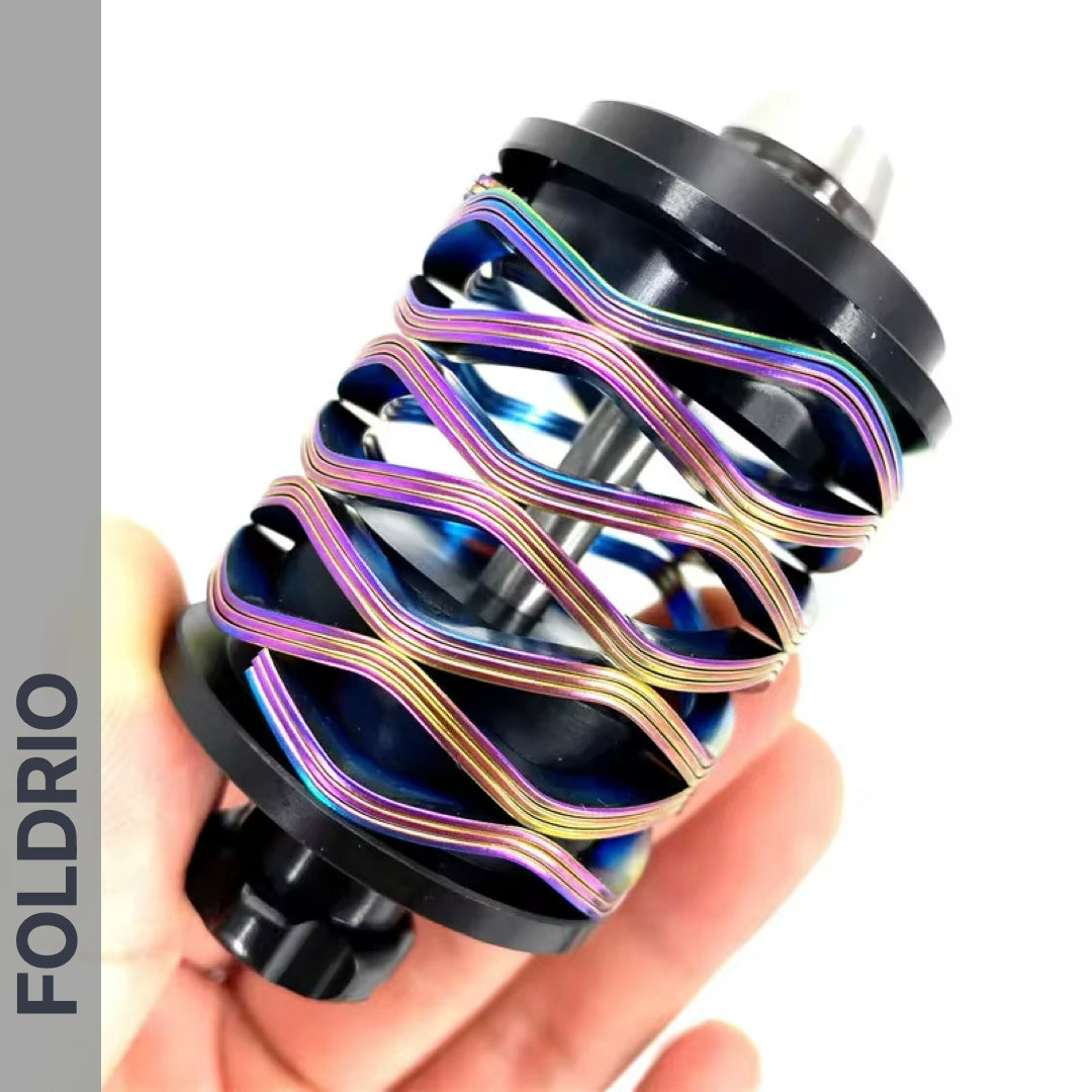 A hand holds a colorful, spiral-shaped Brompton Rear Shock Absorber by FOLDRIO with black end caps and a central rod. The word "FOLDRIO" is displayed vertically on the left side of the image.