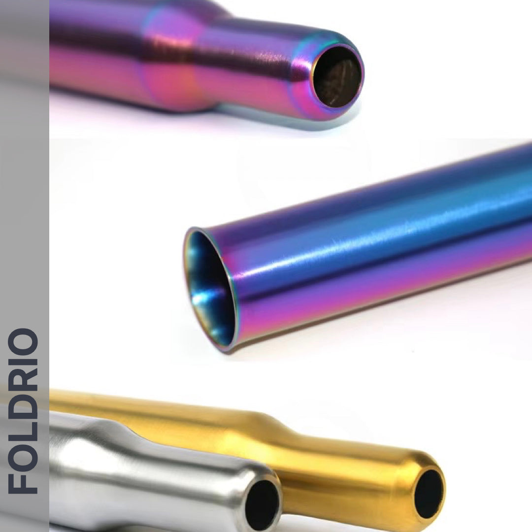 Three metallic, cylindrical Brompton Titanium Seatpost – Multicolour Edition tubes by FOLDRIO are shown in purple-blue, silver, and gold on a white background. The brand name FOLDRIO appears vertically on the left in bold text.