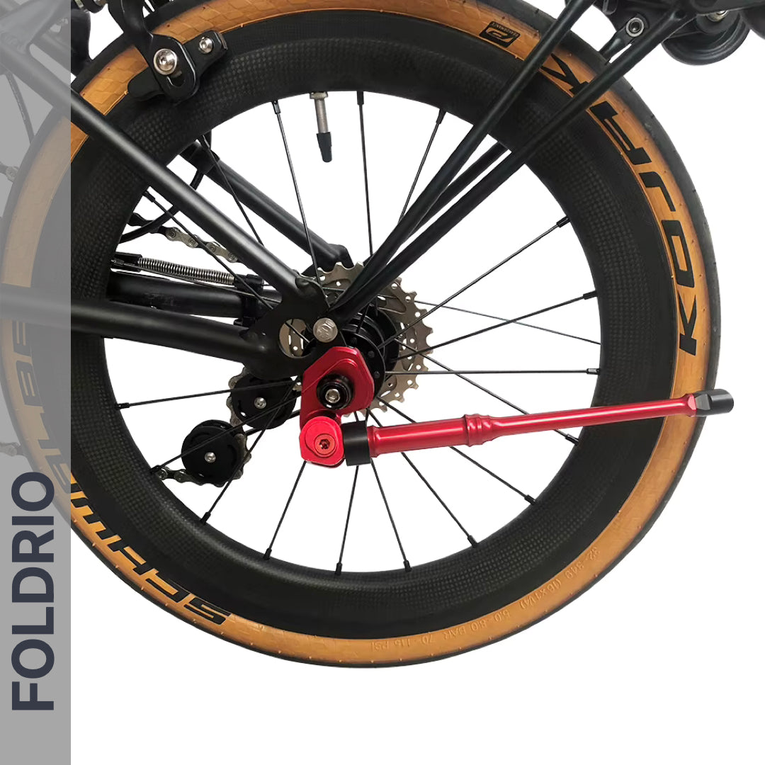 Close-up of a bicycle’s rear wheel featuring a tan Kenda tire, black Shimano derailleur, disc brake, red quick-release lever, and the FOLDRIO Brompton Kickstand – Adjustable Aluminium (A and C Line), with “FOLDRIO” vertically on the left.