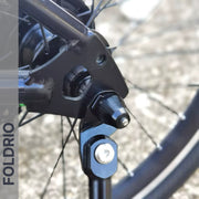 Close-up of a Brompton Kickstand – Carbon Fibre, P and T Line attached to a bike wheel hub; spokes are visible. "FOLDRIO" is displayed vertically on the left side of the image.
