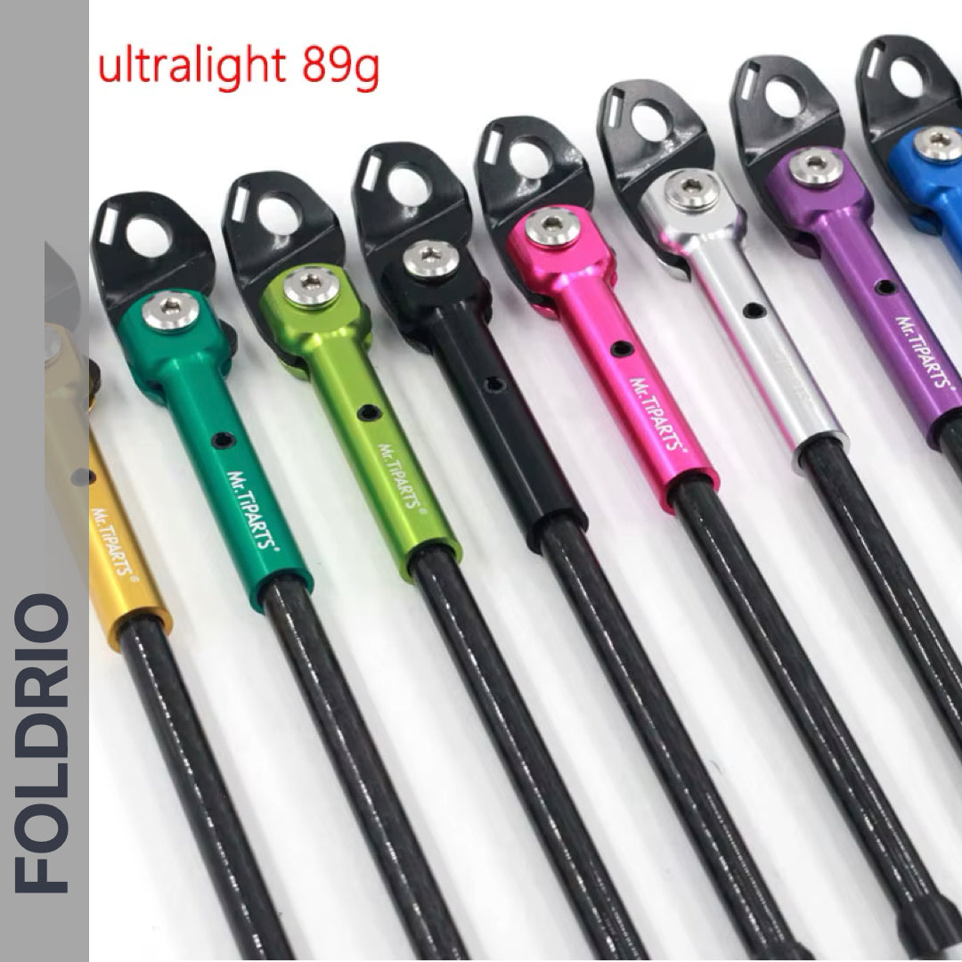 Several colorful Brompton kickstands by FOLDRIO, featuring black heads and ultralight 89g carbon fibre design, are lined up on a white background. "FOLDRIO" appears along the left, highlighting the P and T Line models’ minimal weight.