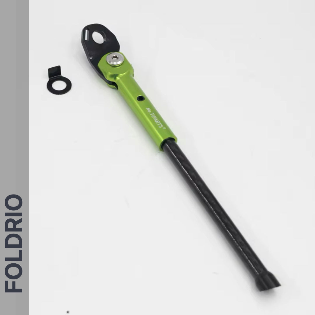 A Brompton Kickstand – Carbon Fibre for P and T Line bikes by FOLDRIO, green and black, adjustable with included washer, is shown on a white background. The word FOLDRIO appears vertically on a sleek grey sidebar.