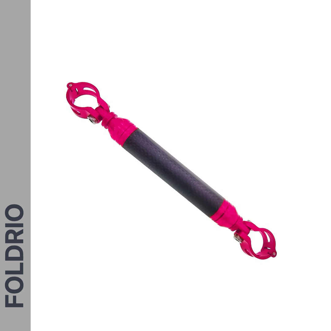 The FOLDRIO Brompton M Handlebar Cross Brace – Adjustable in black and pink with carbon fibre look, clamp attachments at both ends. Shown on a white background with a grey vertical FOLDRIO banner on the left.