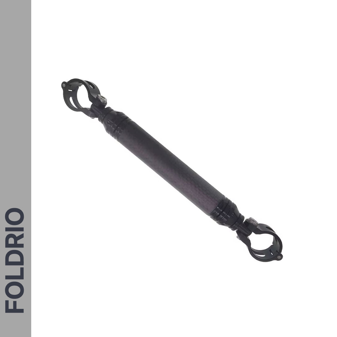The FOLDRIO Brompton M Handlebar Cross Brace—Adjustable and available in 6 colours—appears on a white background with a left gray strip displaying "FOLDRIO" in bold capitals. It’s a black carbon fiber accessory with clamps at both ends.