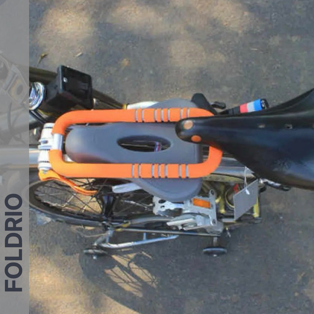 Brompton Brompton folded with orange lock securing seat and frame, front-mounted Foldrio child seat, logo visible on pavement | Foldrio. Foldrio