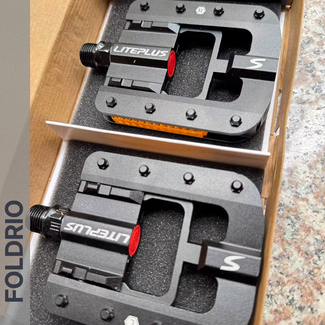 Two black Brompton Foldable Flat Pedals – Lightweight Aluminium Upgrade with metal pins and reflectors are placed in foam in a cardboard box. The word FOLDRIO appears vertically on the image's left side.