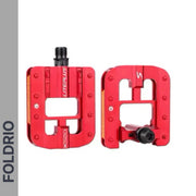 A pair of Brompton Foldable Flat Pedals – Lightweight Aluminium Upgrade with red bodies, black spindles, rectangular open design, and grip pins are shown side by side on a white background. "FOLDRIO" appears vertically on a grey bar to the left.